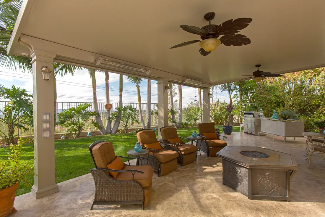 Covered patio with cream columns, ceiling fans, wicker seating, tiled floor, and outdoor fire table