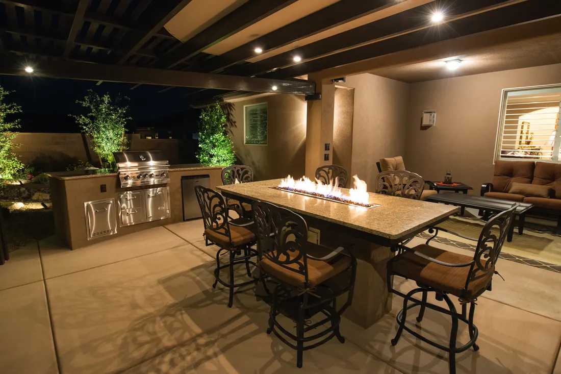 Dark pergola patio cover with recessed lights over an illuminated outdoor kitchen and fire table bar