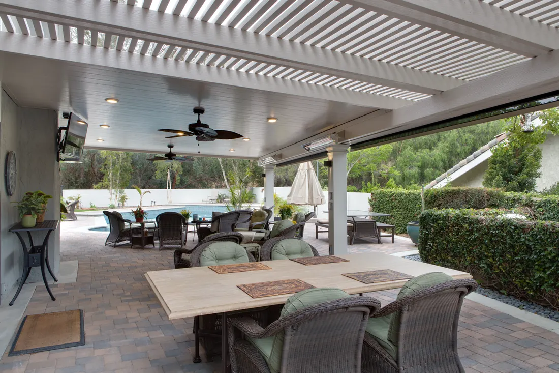 White patio cover with louvered pergola roof, ceiling fans, and outdoor dining next to a pool