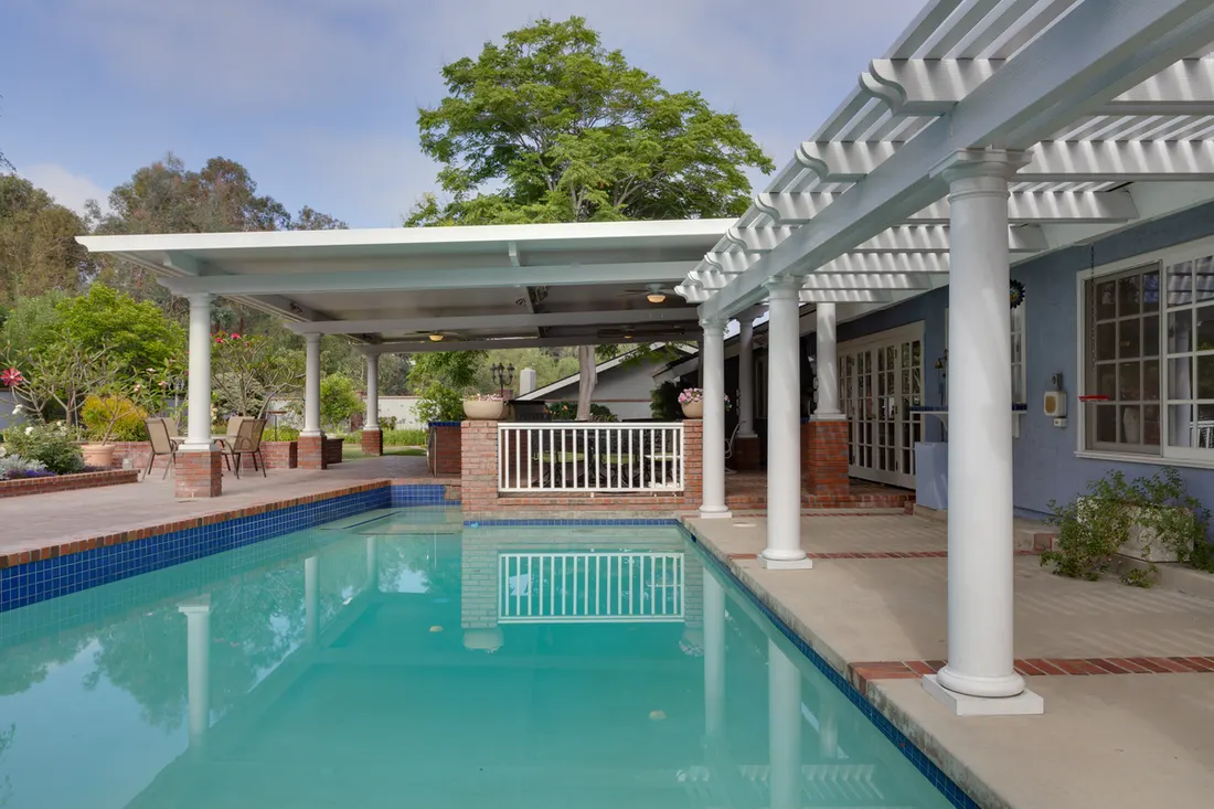 White patio cover with pergola beams and columns beside a turquoise swimming pool