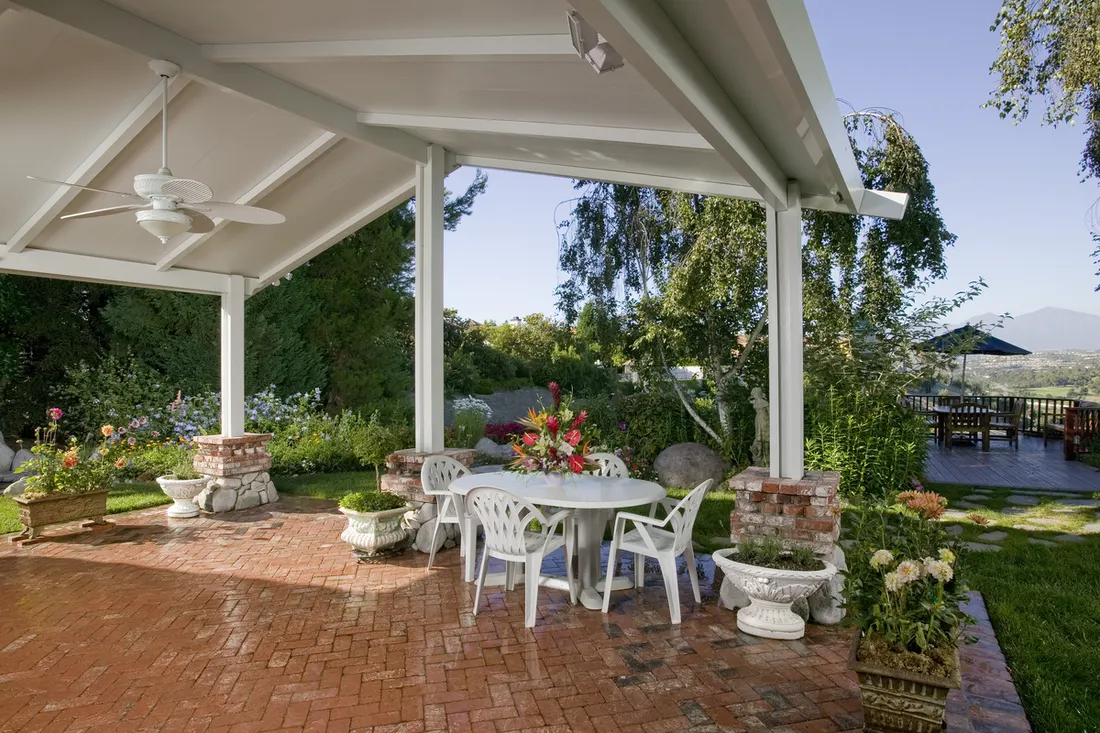 White gabled patio cover with posts on brick bases over a red brick patio