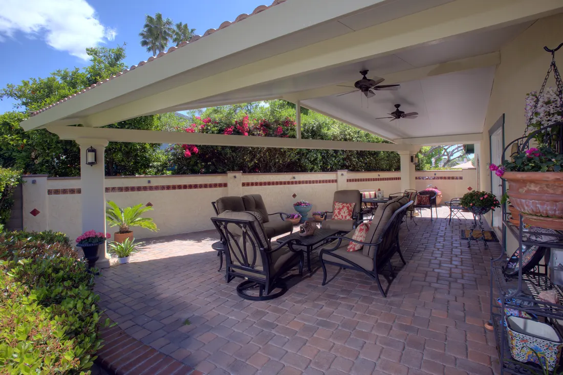 Cream patio cover with ceiling fans over a brick paver courtyard with outdoor furniture