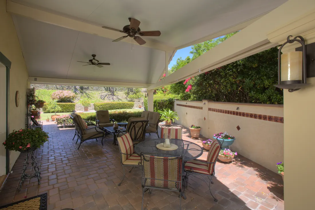 Cream solid patio cover with ceiling fans sheltering a brick patio with outdoor furniture