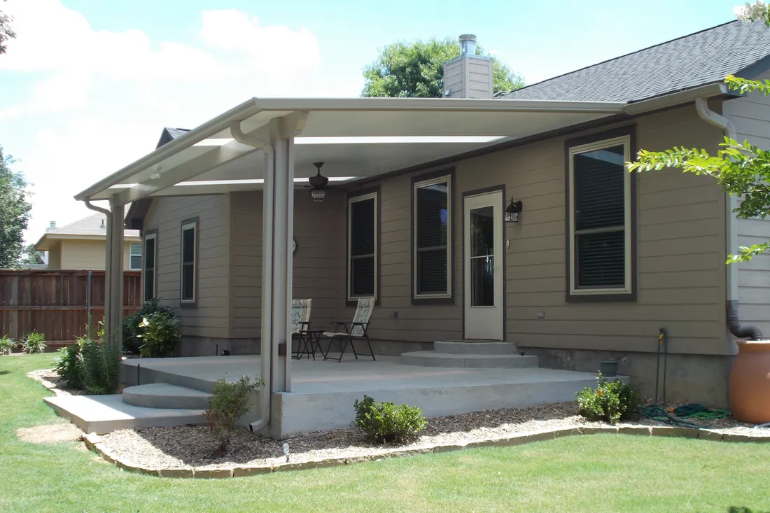 Covered patio with gray roof, white columns, concrete slab, beige siding, and lawn