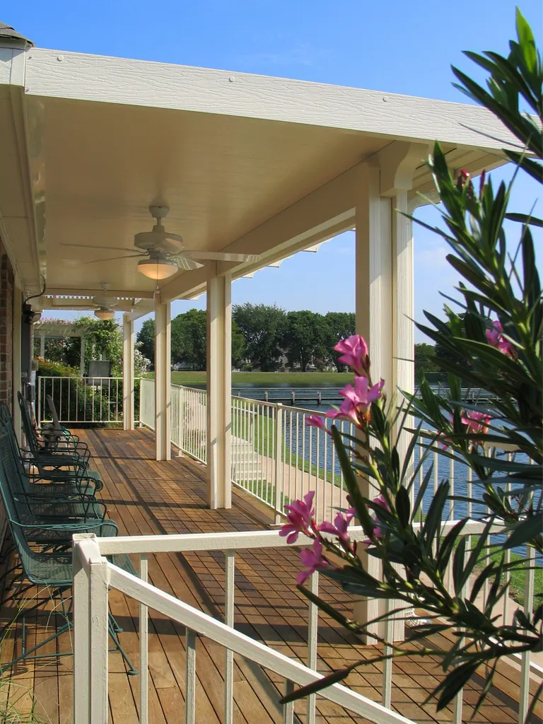 Cream solid patio cover with ceiling fans over a wooden deck overlooking a lake waterfront