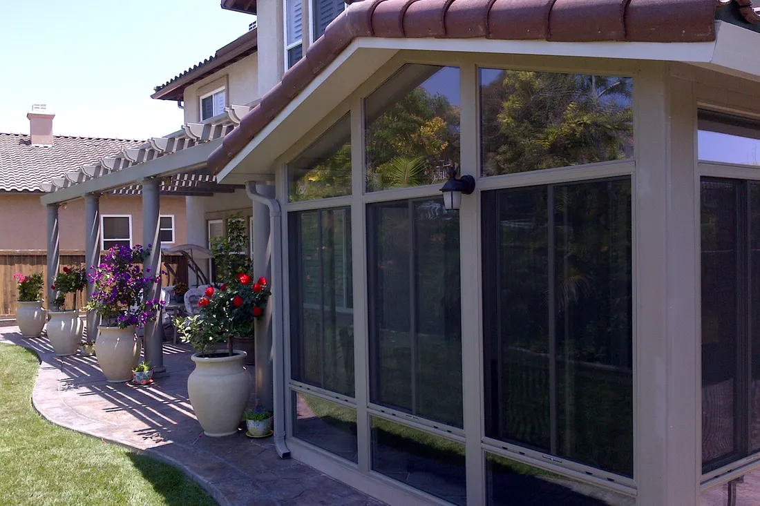 Glass patio enclosure with tile roof attached to house beside a pergola and stone walkway