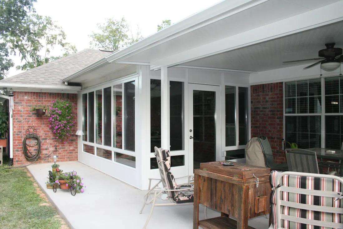White-framed screened patio enclosure with glass doors, brick walls, ceiling fan, and outdoor seating