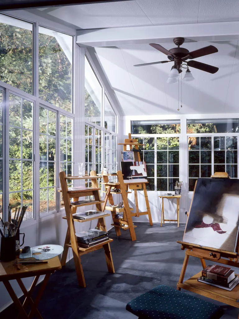 Enclosed sunroom patio with large white-framed windows, vaulted ceiling, and wooden art studio easels