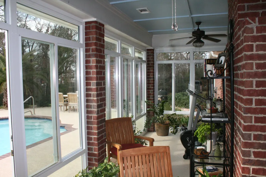 Enclosed patio with brick columns, large white-framed windows, blue ceiling, and outdoor pool view
