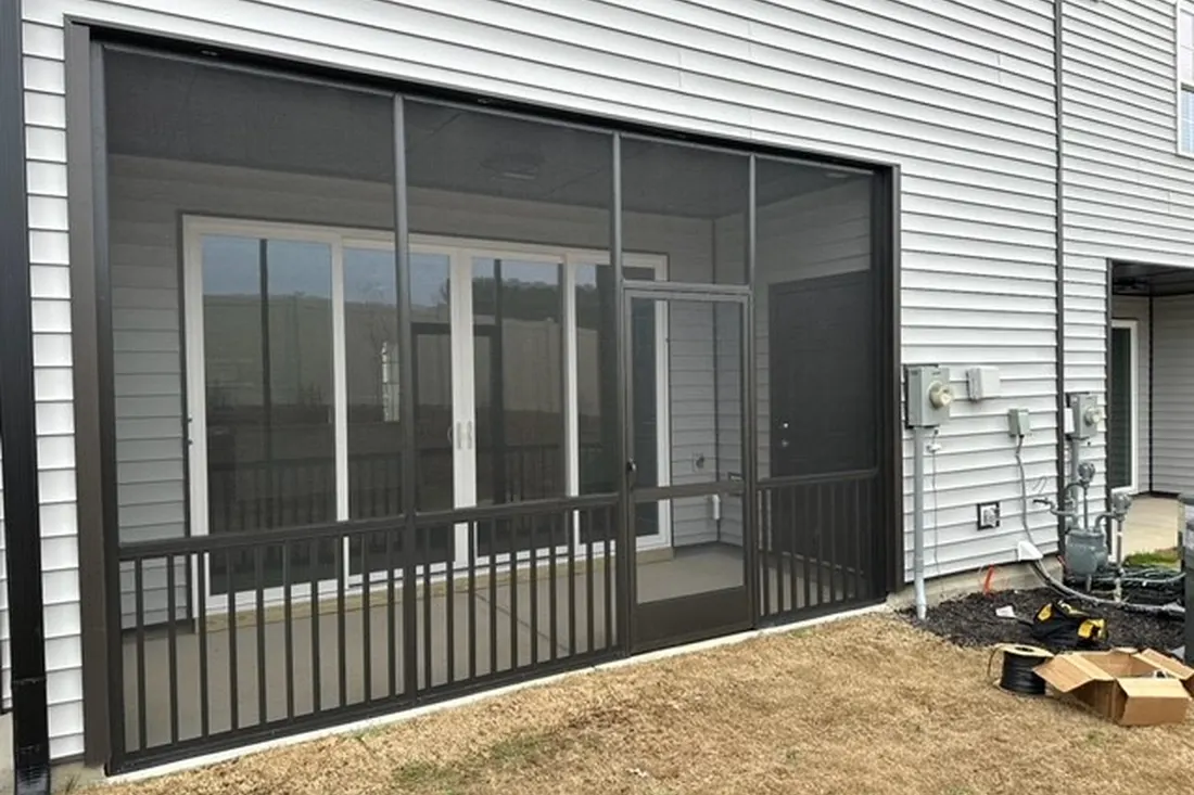Dark brown aluminum screened-in patio enclosure with railing panels attached to a light gray house