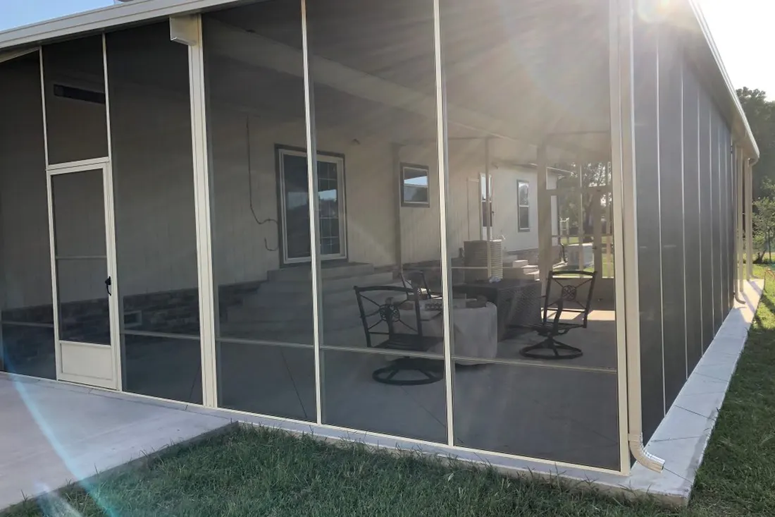 Screened-in patio enclosure with cream aluminum frame, mesh walls, and concrete foundation beside green lawn