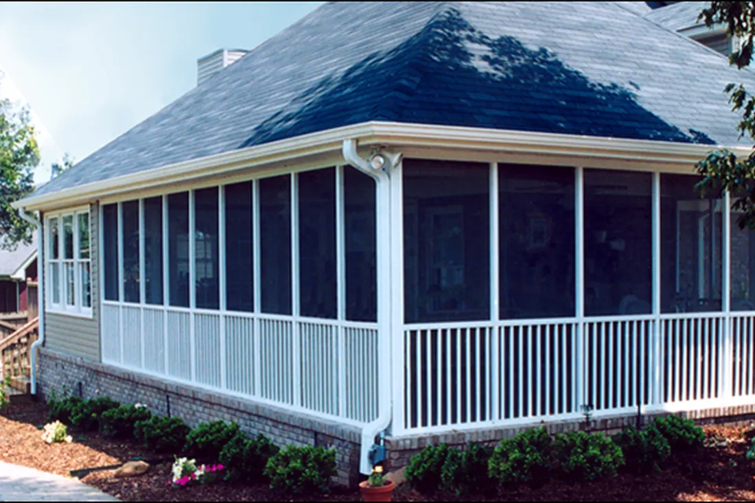 Screened patio enclosure with white railings, gray roof, brick foundation, and landscaped shrubs