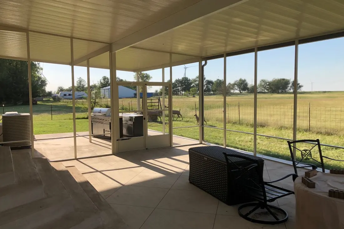 Cream screened-in patio enclosure with tiled floor overlooking a sunny grassy rural yard