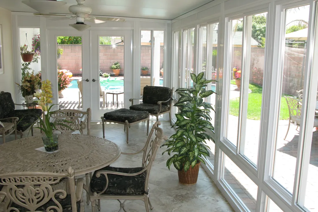 White framed sunroom enclosure with large glass windows overlooking a backyard pool and patio
