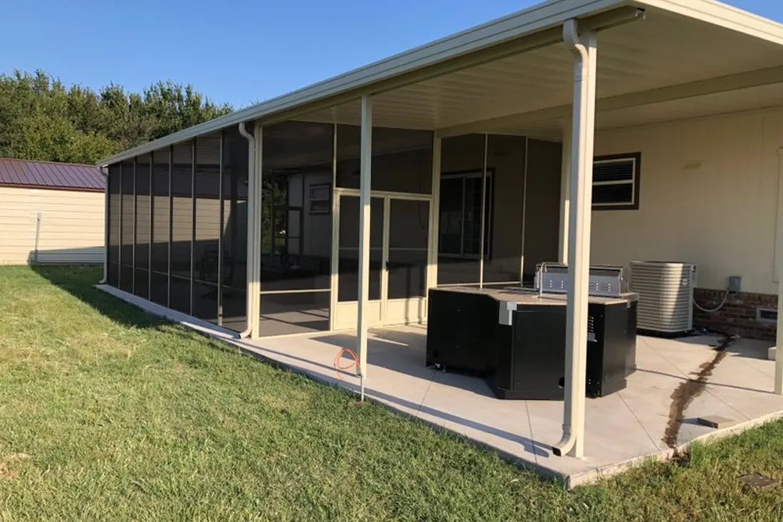 Screened-in patio enclosure with beige aluminum awning and concrete patio beside a grassy lawn