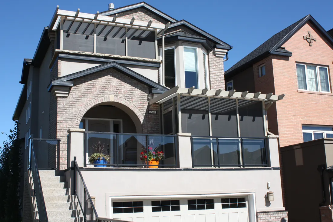 Glass-enclosed patio with dark frames and pergola roof on a gray brick townhouse