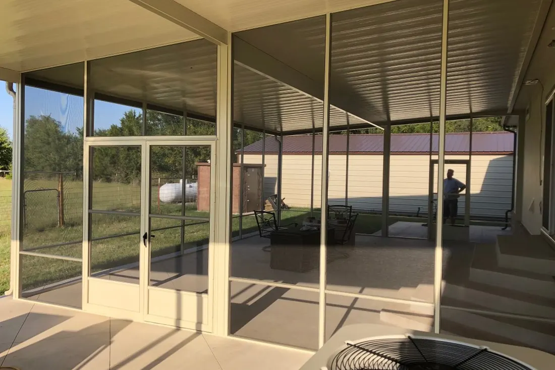 Screened patio enclosure with beige aluminum framing, mesh panels, concrete floor, and adjacent lawn