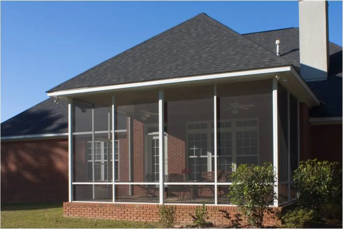 Screened patio enclosure with white framing and dark shingled roof on red brick house