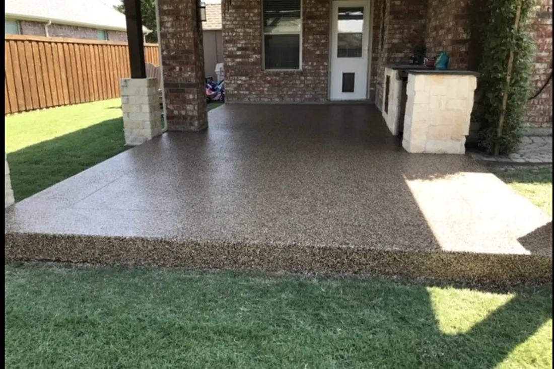 Textured patio floor coating covering a covered brick porch, with stone columns and a backyard lawn