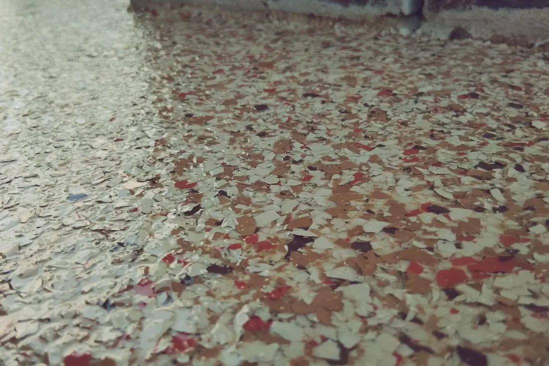 Close-up of glossy patio floor coating with multicolored decorative red, tan, and white flakes