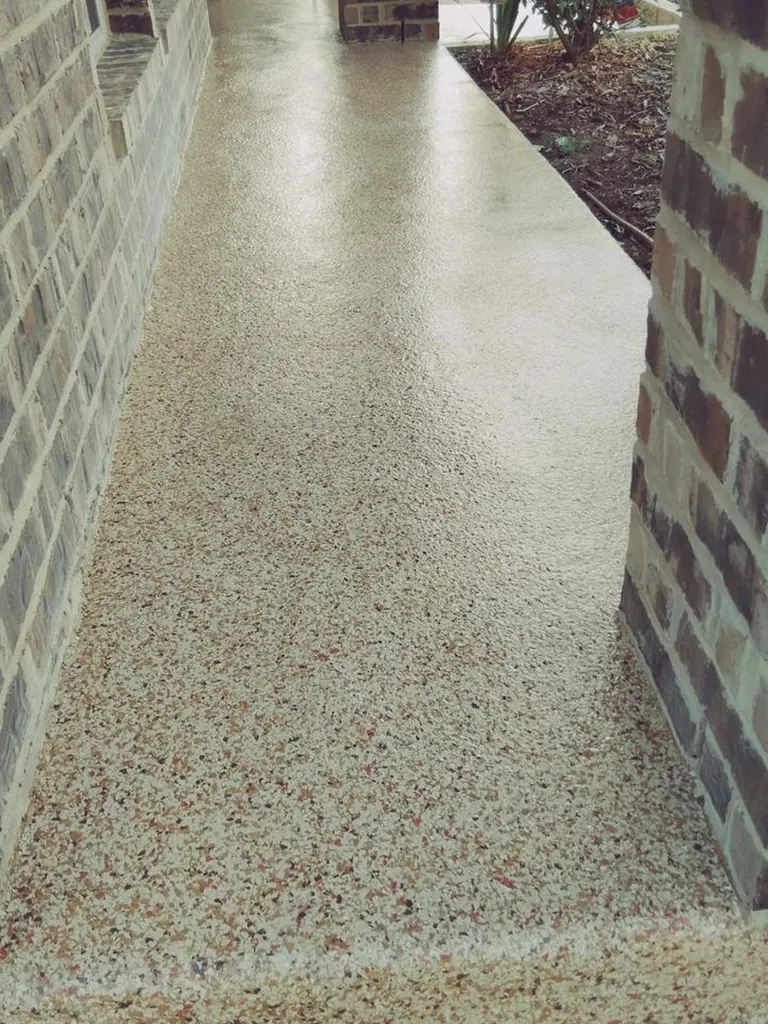 Speckled light-colored coated patio walkway between brick walls and landscaped soil