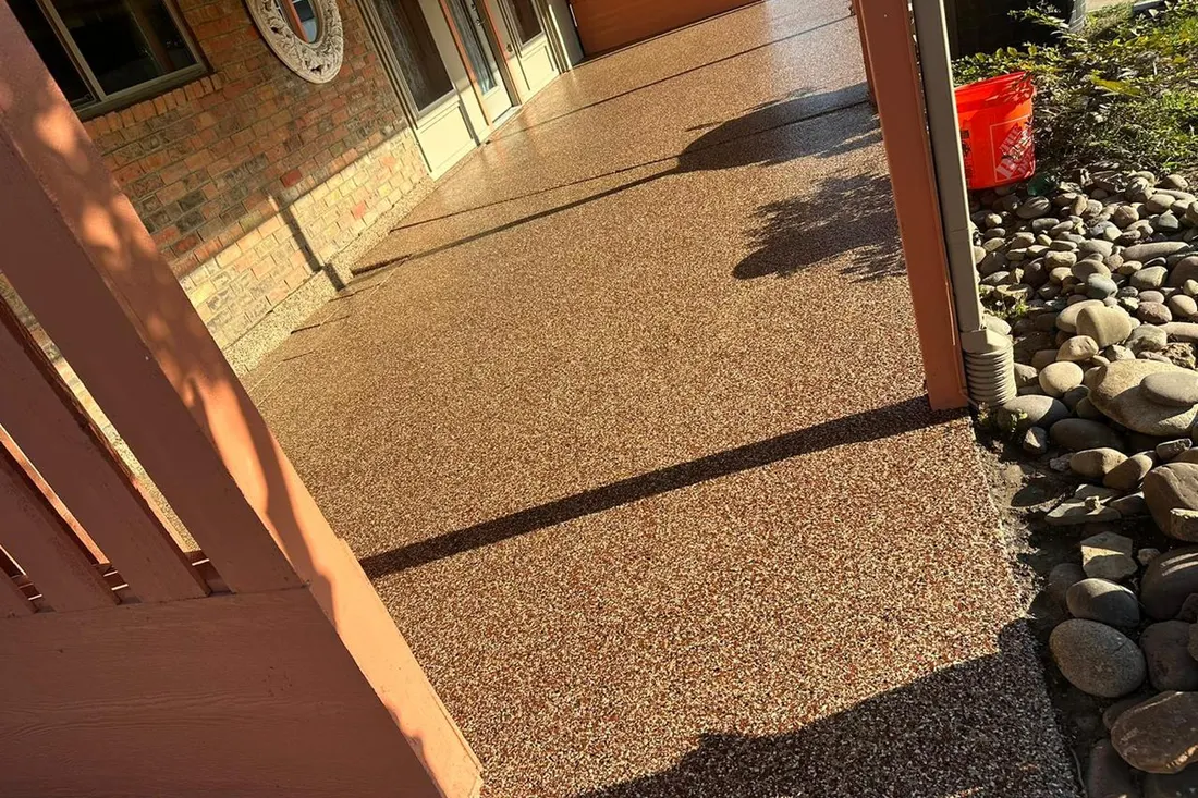 Textured brown patio floor beside a brick house, with wood posts and river rocks
