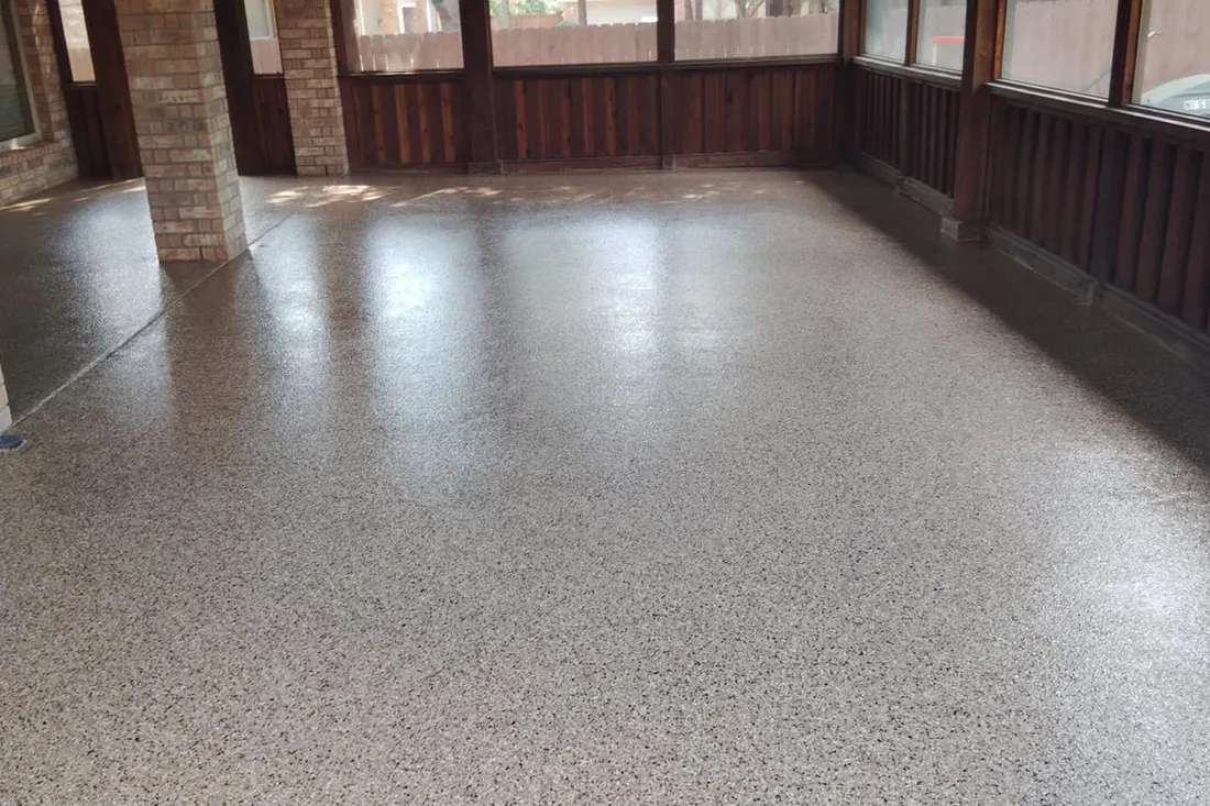 Speckled gray coated patio floor enclosed by brick columns, dark wood paneling, and windows