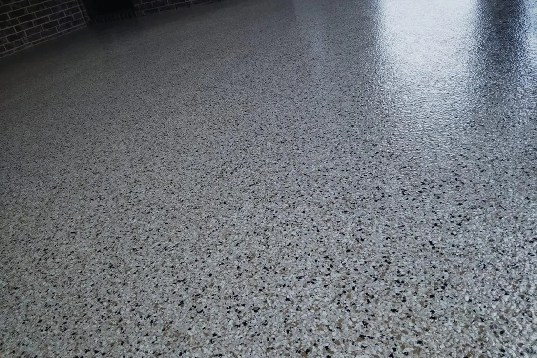 Speckled gray patio floor coating with a smooth, textured finish beside a dark brick wall