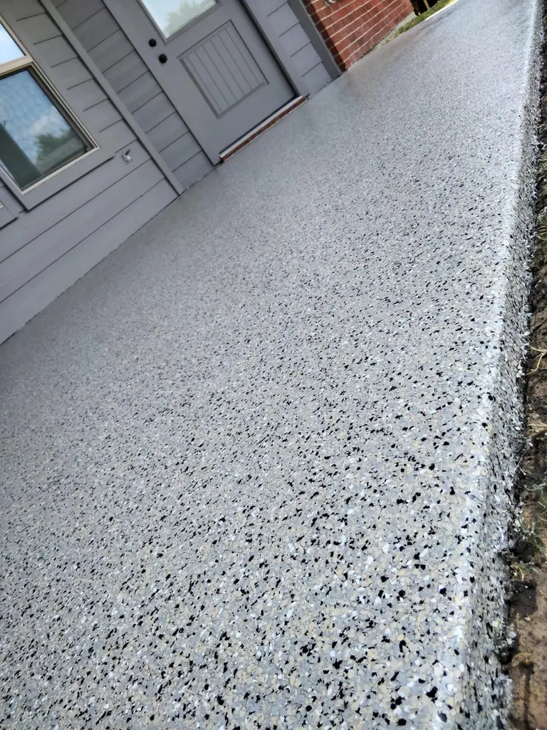 Speckled light gray patio floor coating beside gray siding and a door next to brick siding