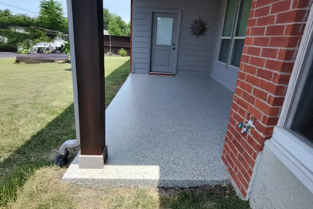 Gray speckled coated concrete patio floor beside red brick wall and wooden support pillar outdoors