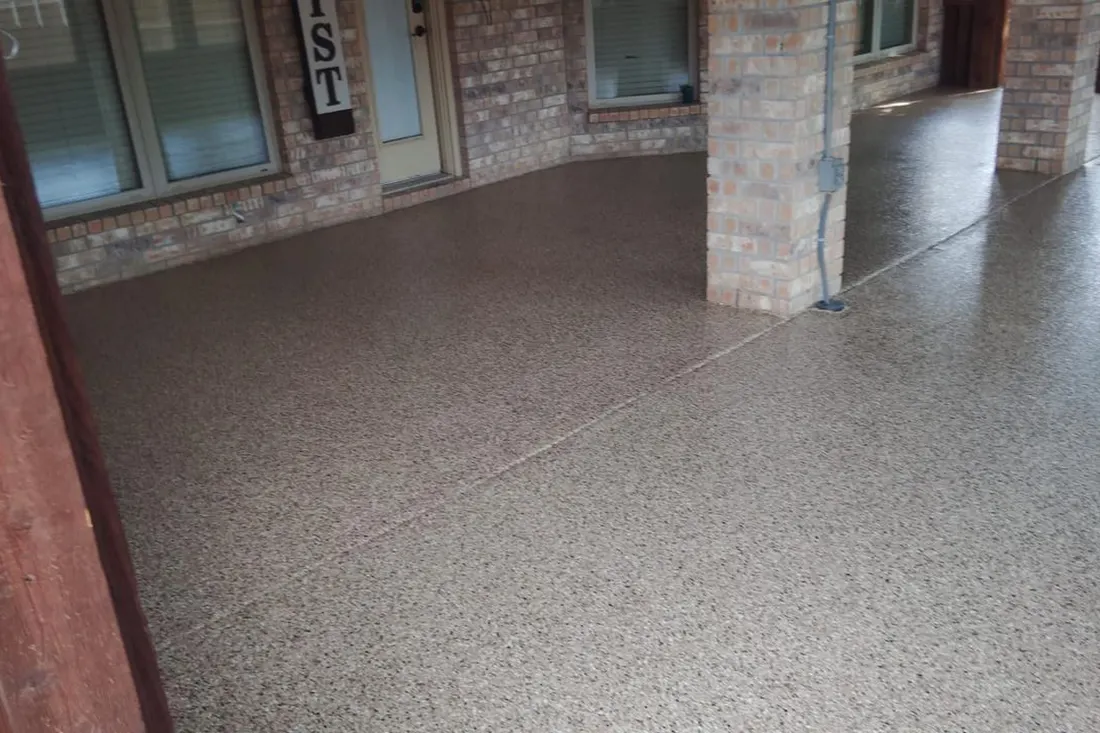 Speckled brown and gray coated concrete patio beneath a brick-covered porch with square columns