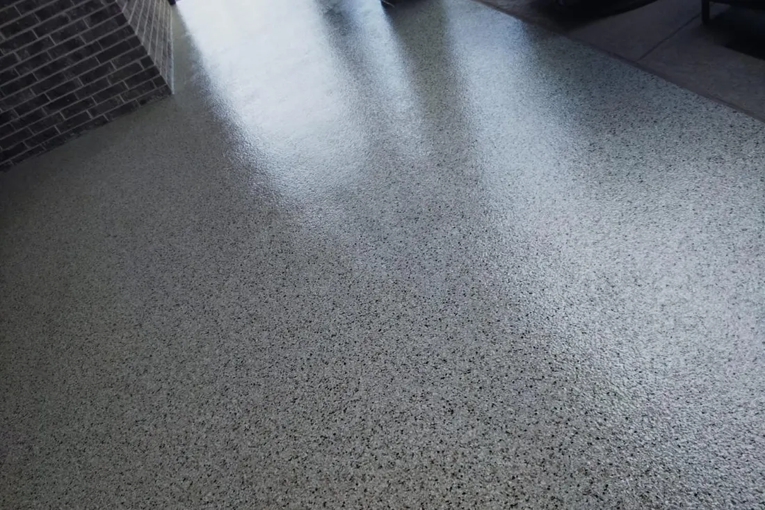 Speckled gray patio floor coating beside a dark brick wall under a covered patio