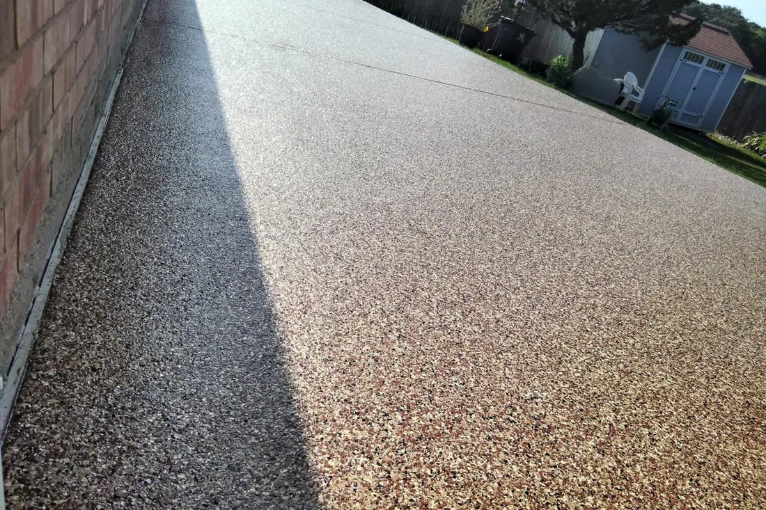 Speckled brown and beige coated concrete patio floor extending along a red brick house wall