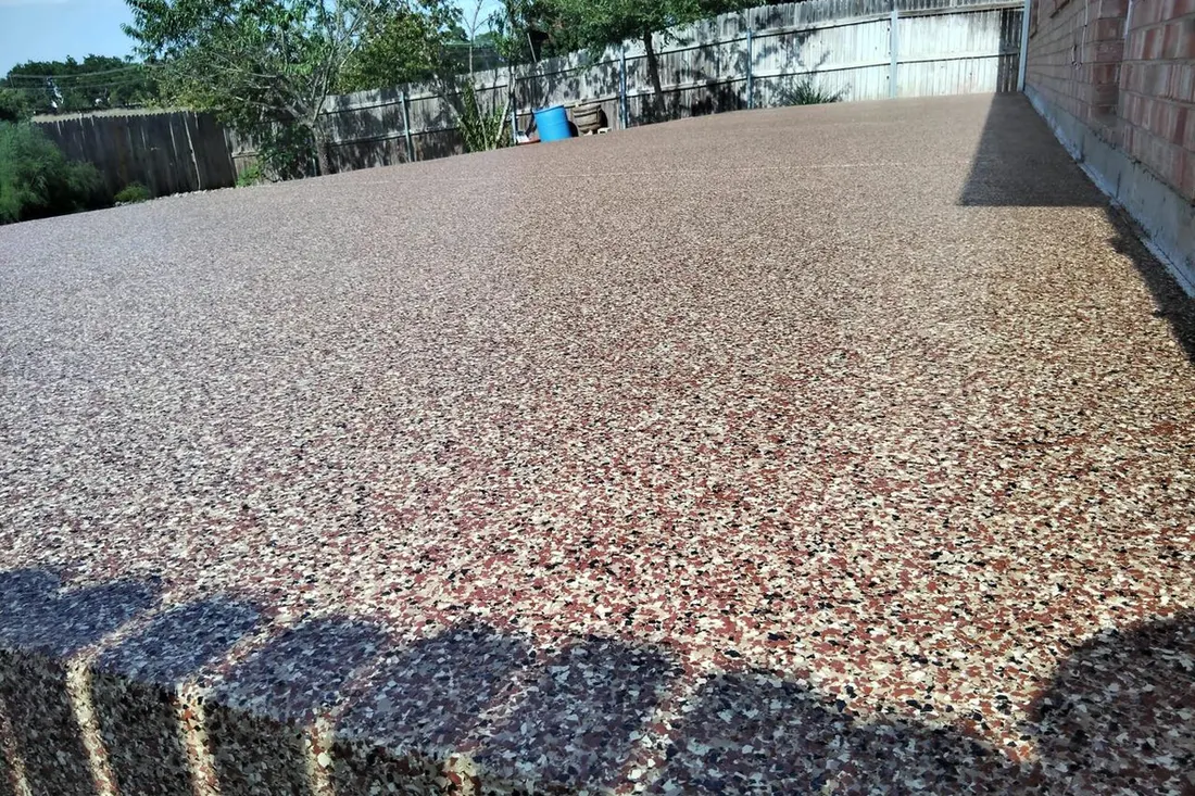 Speckled red and gray coated patio floor beside a brick wall and fenced backyard