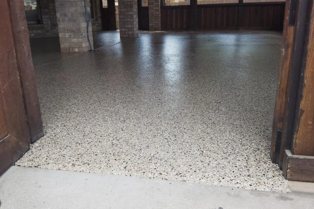 Speckled light gray coated patio floor inside a covered wooden structure with brick columns