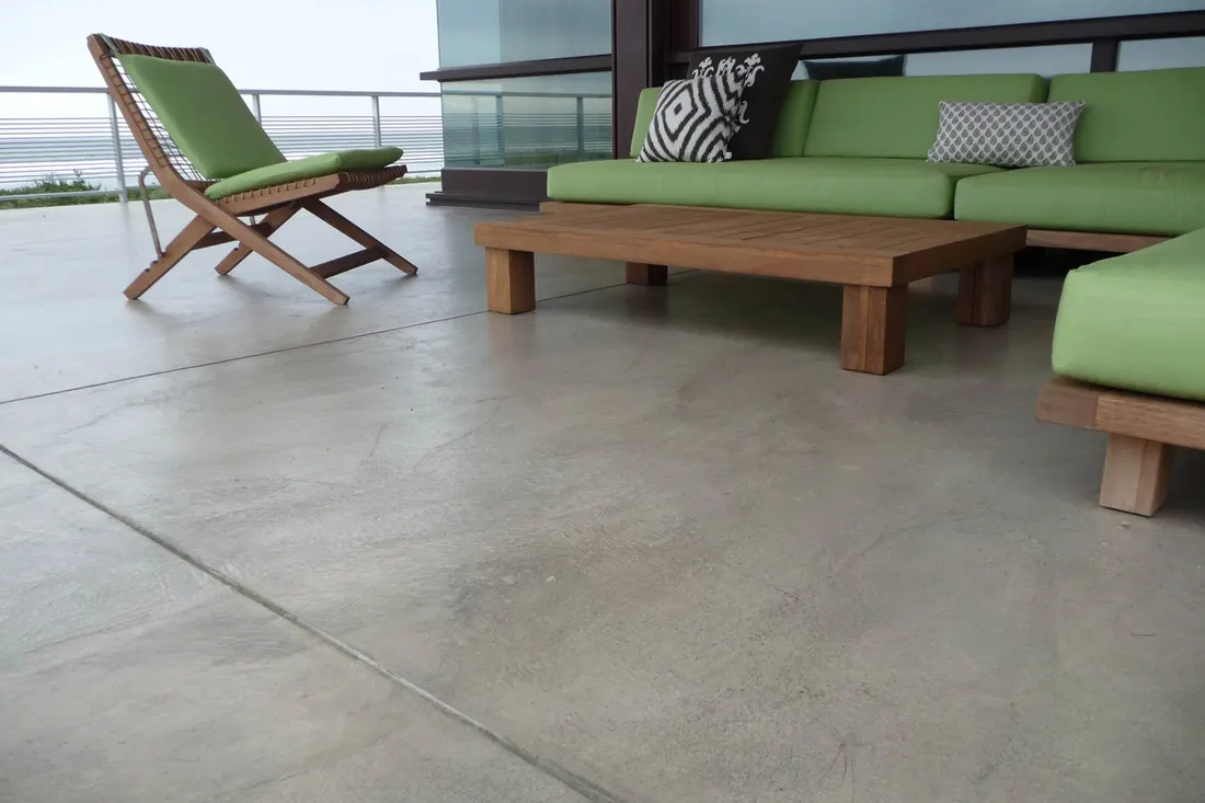 Smooth coated concrete patio floor with green cushioned wooden outdoor furniture and coastal views