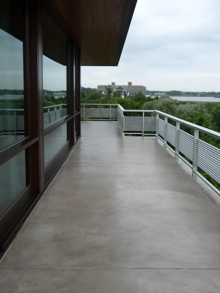 Gray coated concrete patio with metal railings overlooking greenery, houses, and a body of water