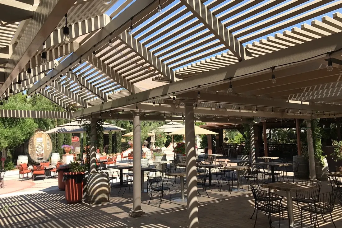 Wooden pergola with slatted roof shading an outdoor patio filled with tables and chairs