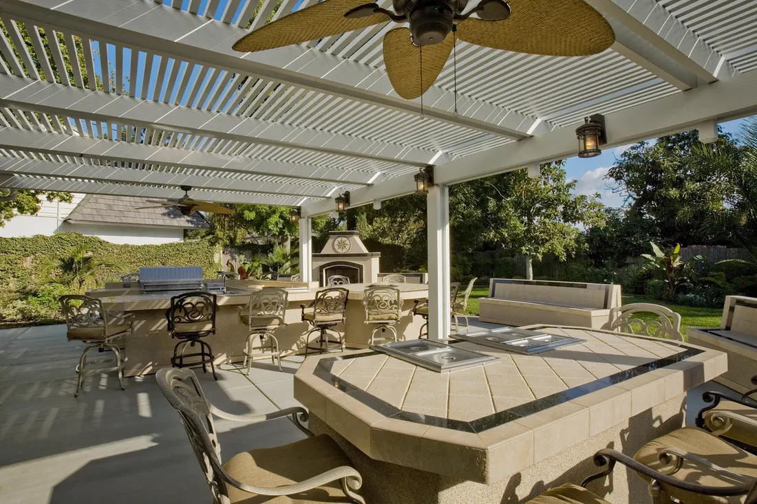 White slatted pergola over a tiled outdoor patio with ceiling fan, furniture, and garden