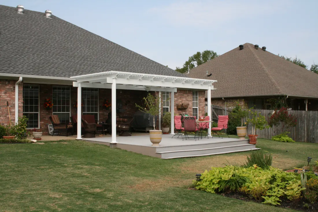 White vinyl pergola over a raised backyard patio deck behind a brick house