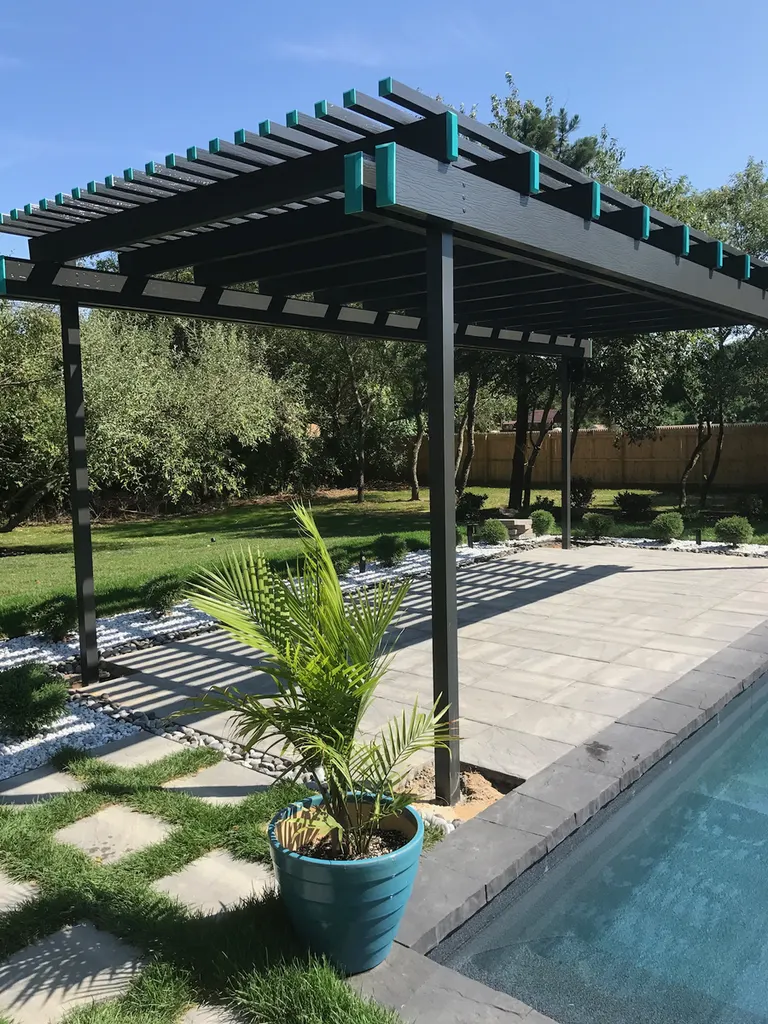 Dark wood pergola with slatted roof beside a tiled patio, pool, lawn, trees, and potted palm