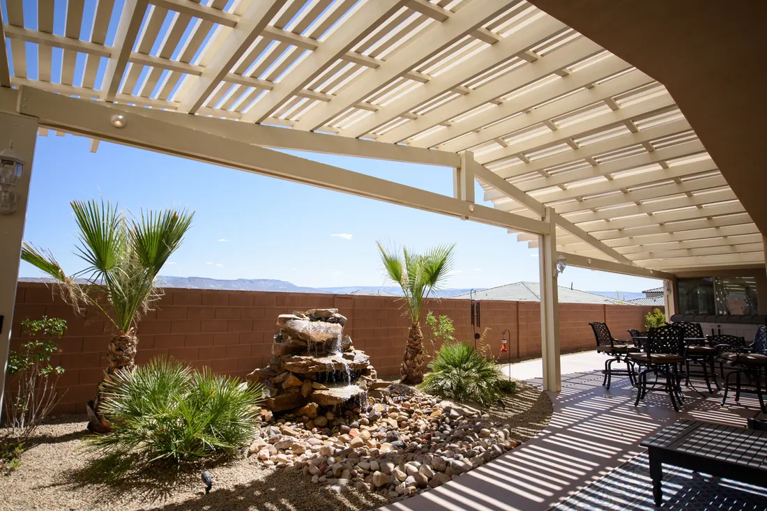 White pergola with slatted roof, desert landscaping, rock waterfall, patio furniture, and mountain views