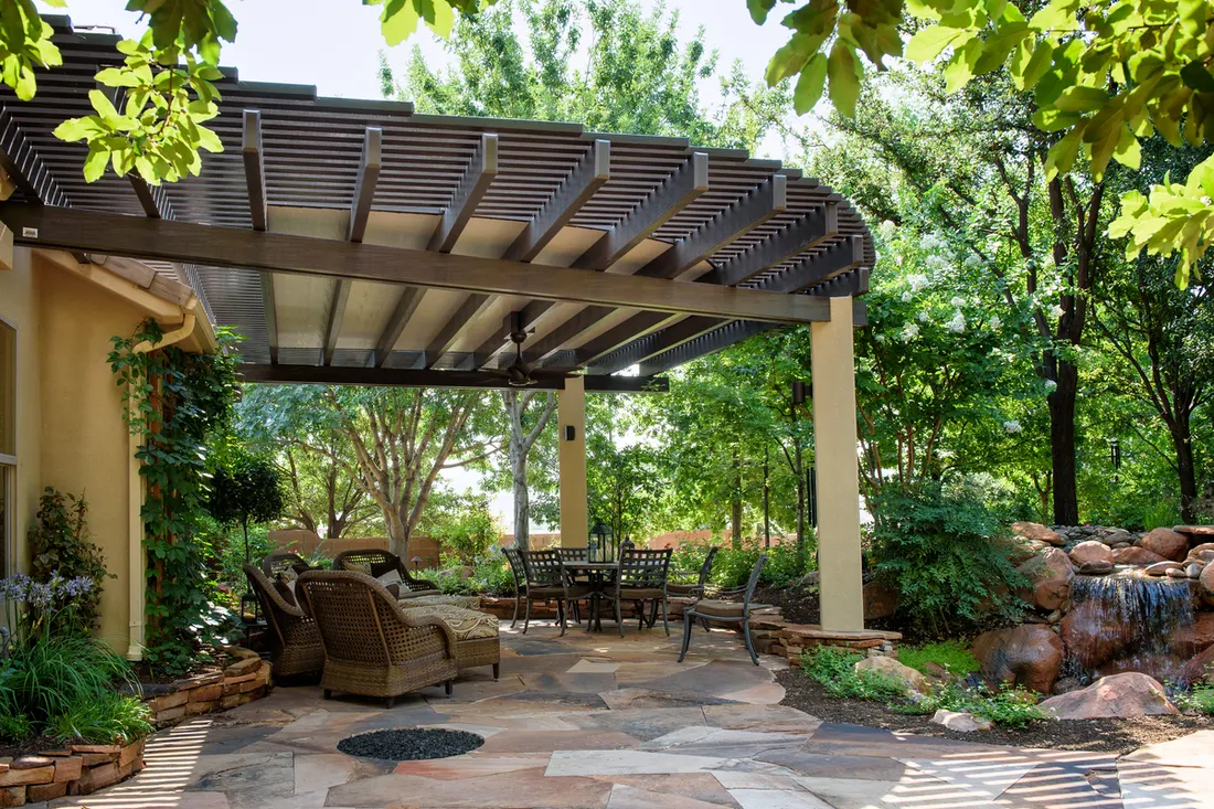 Curved dark brown pergola over a flagstone patio with outdoor seating in a lush backyard