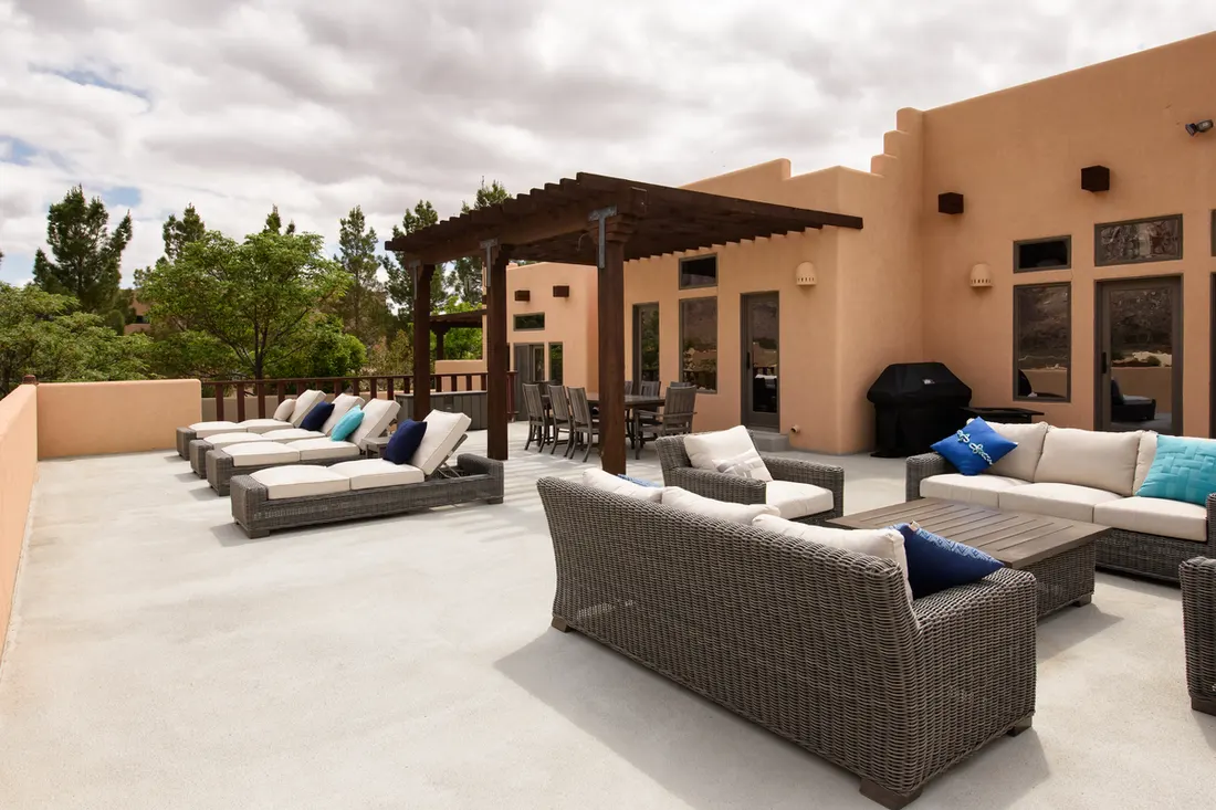Dark wood pergola shading a patio dining set on an expansive adobe house terrace