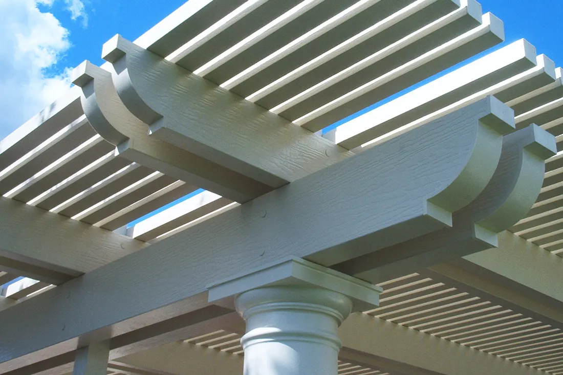 White pergola with slatted beams, decorative curved brackets, and column against a blue sky