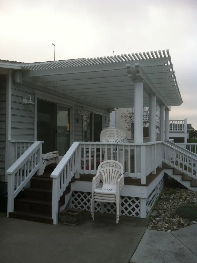 Attached white wooden pergola covering a raised back deck with railings and steps