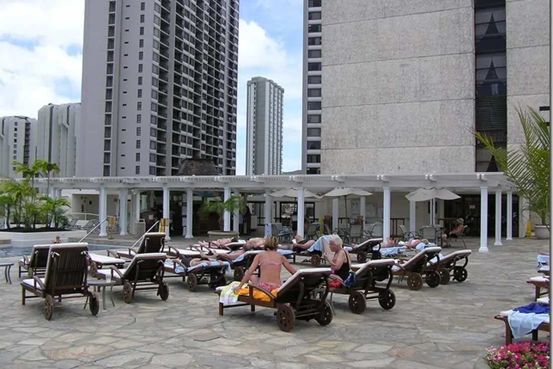 White pergola with columns and slatted roof beside lounge chairs on a paved urban terrace