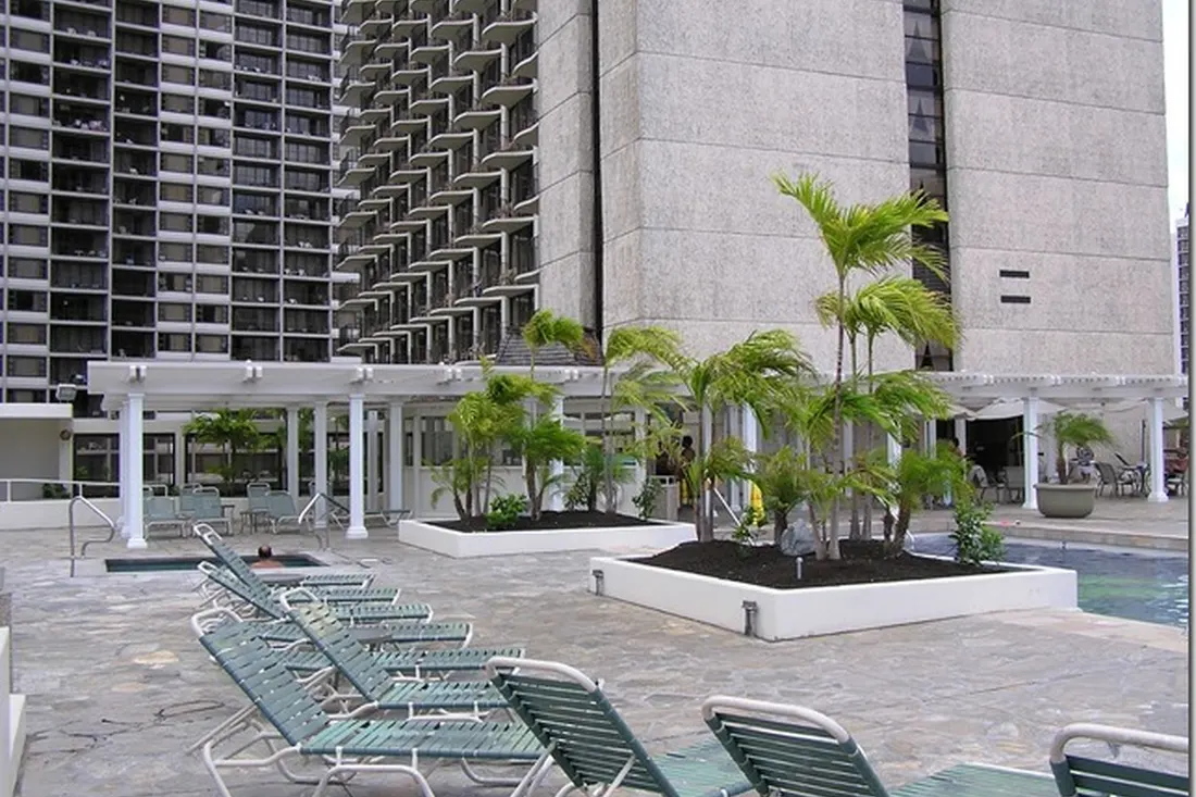 White pergola with square columns beside palm planters and poolside lounge chairs