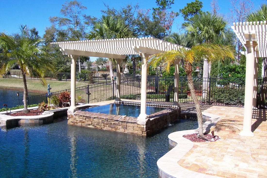 White pergola with columns over a raised stone spa within a backyard swimming pool