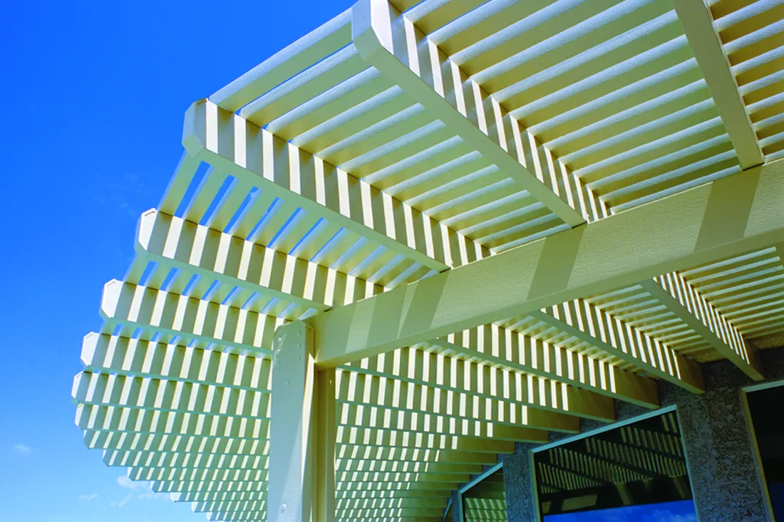 Curved white pergola structure with slatted beams attached to a building against blue sky